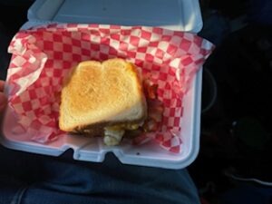 A person holding a sandwich inside a white container, showcasing the meal ready to be enjoyed.