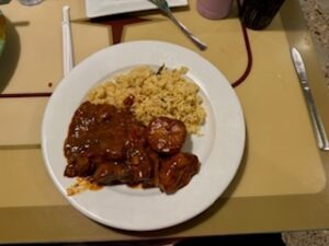 A plate featuring a cooked steak, seasoned potatoes, and a glass of water beside it.