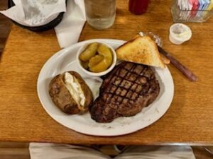 A plate featuring a cooked steak, seasoned potatoes, and a glass of water beside it.