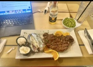 A plate of steak and potatoes sits on a table next to a laptop, creating a cozy dining and work environment.